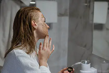 person putting coffee scrub on face